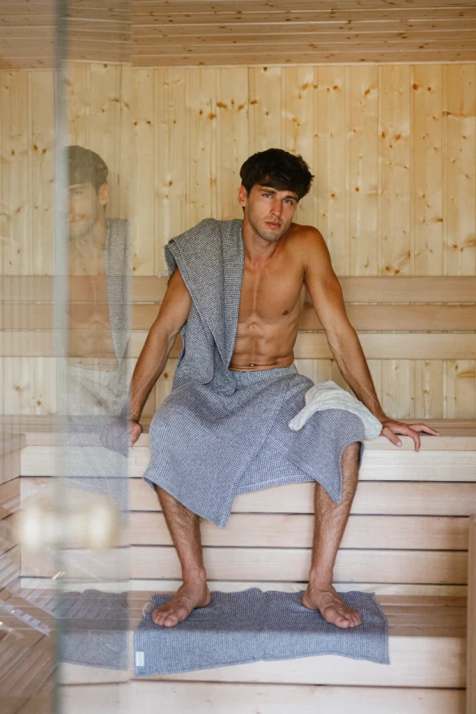 mężczyzna siedzący w saunie ubrany w lniany kilt i owinięty ręcznikiem lnianym wafel natural jeans